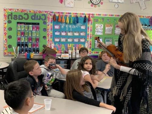 An LC student teacher shows students a violin.